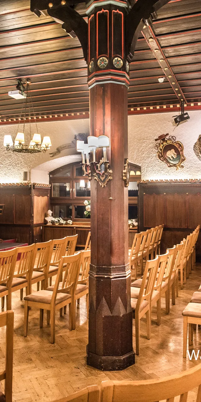 Konzertsaal mit Holzstühlen, Flügel, Bühnenbeleuchtung und mittelalterlichen Wappen